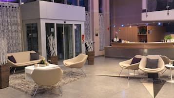 A modern lobby with seating areas, a reception desk, and a glass partition.
