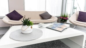 A modern, minimalist living area with a white coffee table, two armchairs, a sofa, and a potted plant. - elaya hotel wolfenbuettel, Trademark Collection by Wyndham (Wolfenbuettel)
