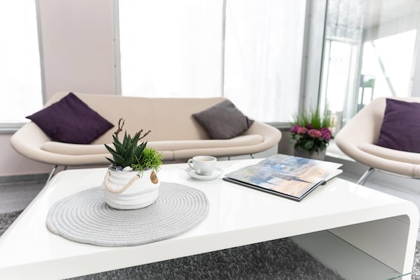 A modern, minimalist living area with a white coffee table, two armchairs, a sofa, and a potted plant. - elaya hotel wolfenbuettel, Trademark Collection by Wyndham (Wolfenbuettel)