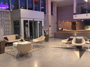 A modern lobby with seating areas, a reception desk, and a glass partition. - elaya hotel wolfenbuettel, Trademark Collection by Wyndham (Wolfenbuettel)