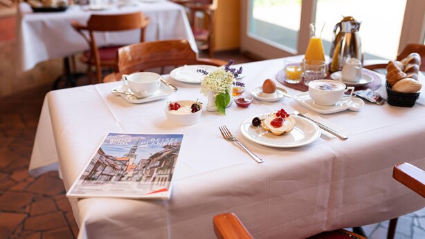 A breakfast table set with plates, cups, and a menu. - elaya hotel wolfenbuettel, Trademark Collection by Wyndham (Wolfenbuettel)