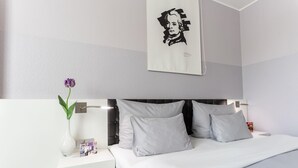 A modern hotel room with a large bed, white bedding, a nightstand with a vase of flowers, and a framed artwork on the wall. - elaya hotel wolfenbuettel, Trademark Collection by Wyndham (Wolfenbuettel)