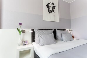 A modern hotel room with a large bed, white bedding, a nightstand with a vase of flowers, and a framed artwork on the wall. - elaya hotel wolfenbuettel, Trademark Collection by Wyndham (Wolfenbuettel)