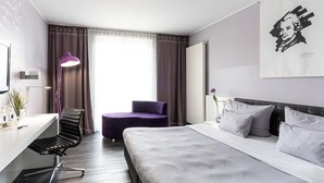 A modern hotel room with a bed, a desk, a chair, and a large window with curtains. - elaya hotel wolfenbuettel, Trademark Collection by Wyndham (Wolfenbuettel)