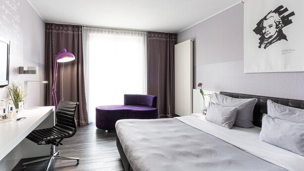 Una habitación de hotel moderna con cama, escritorio, silla y un ventanal con cortinas.