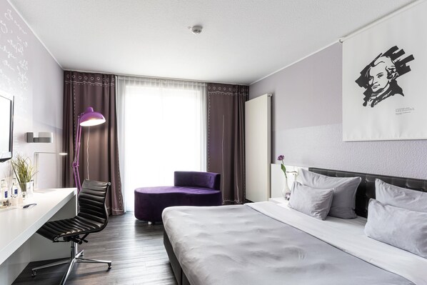 A modern hotel room with a bed, a desk, a chair, and a large window with curtains. - elaya hotel wolfenbuettel, Trademark Collection by Wyndham (Wolfenbuettel)