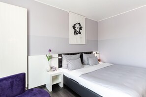 A modern hotel room with a large bed, a nightstand, a purple chair, and a wall-mounted artwork. - elaya hotel wolfenbuettel, Trademark Collection by Wyndham (Wolfenbuettel)