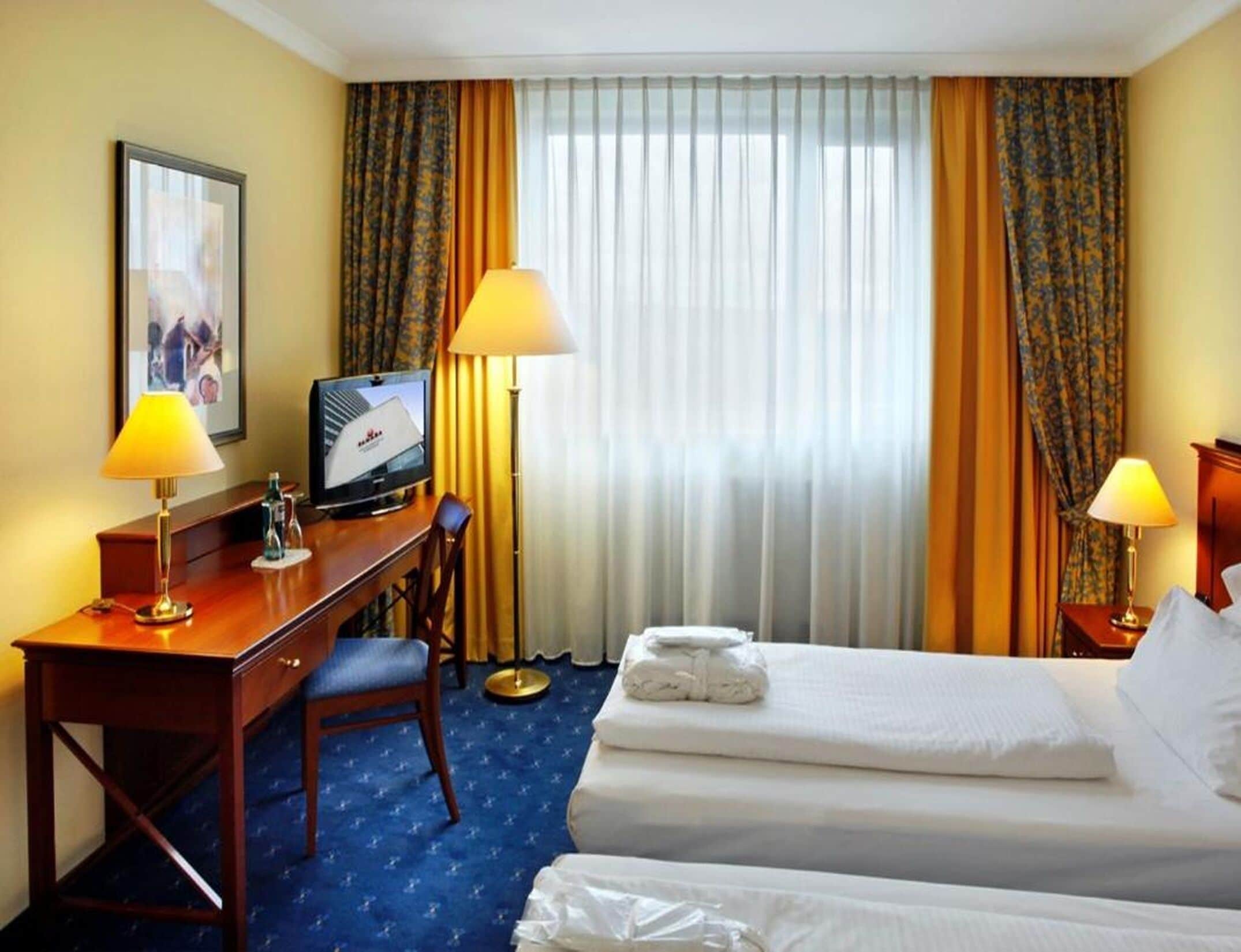 A hotel room with a desk, two beds, a television, and a window with curtains.