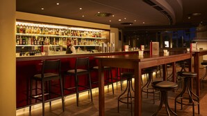Zona de bar con varios taburetes, una barra repleta de botellas y una persona sirviendo.