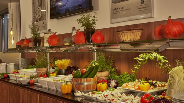 A buffet with various food items and decorative plants. - Sunday Hotel Kassel (Kassel)