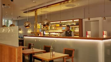 A bar area with a counter, shelves of bottles, and hanging pendant lights.