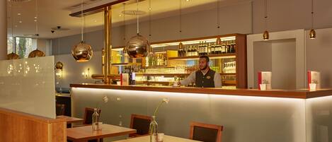 Eine Bar mit einer Theke, Flaschenregalen und hängenden Pendelleuchten.