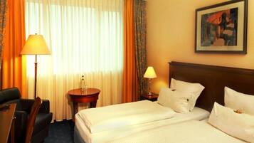 A hotel room with two beds, a desk, a chair, a lamp, and a painting on the wall.