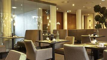 A modern hotel dining area with tables and chairs, ambient lighting, and a view of the interior.