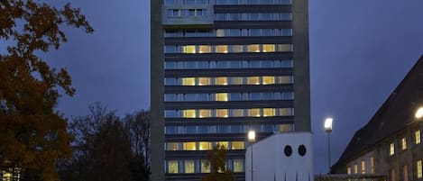 Un hôtel à plusieurs étages, doté d’une façade moderne, de grandes fenêtres et d’un parking où sont stationnées des voitures.