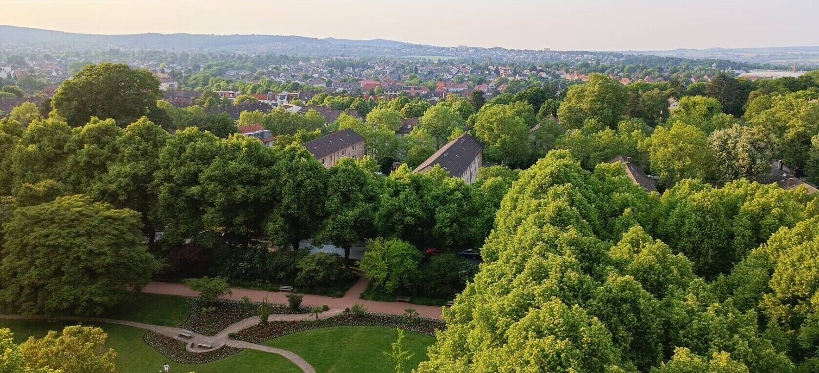 An aerial view of a residential area with houses, trees, and a park with a pathway.