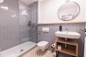 Un baño moderno con cabina de ducha de vidrio, inodoro, lavabo con espejo sobre él y baldosas de suelo estampadas.