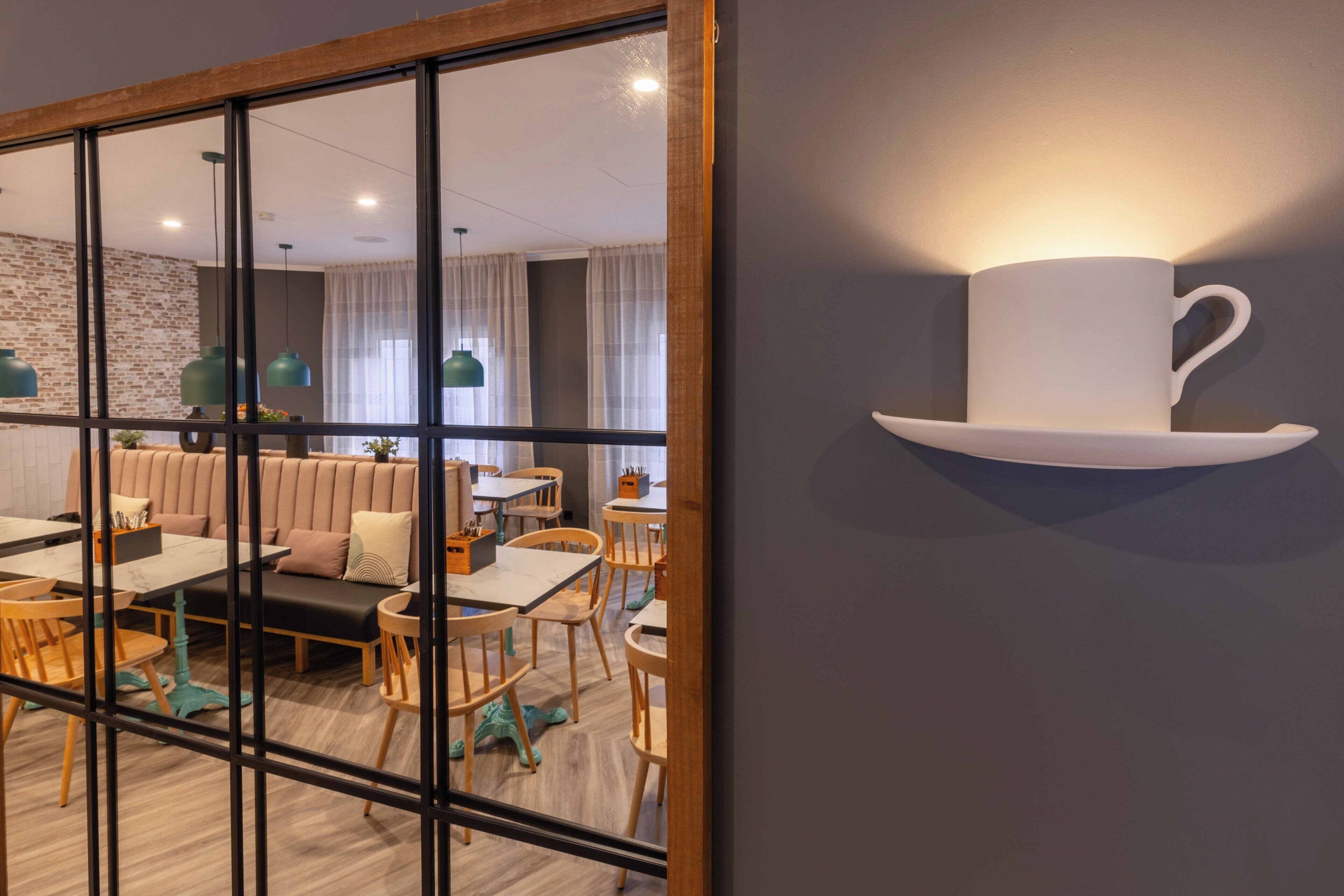 A modern dining area with a glass partition, wooden furniture, and a wall-mounted cup holder.