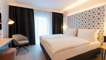Camera d'albergo con un letto grande, una scrivania, una sedia e un muro con motivo geometrico.