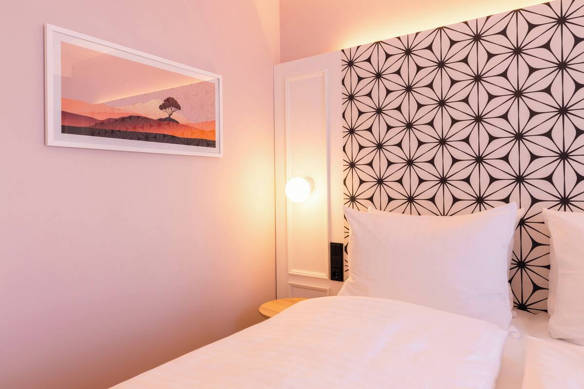 Ein Schlafzimmer mit einem Bett, einem Nachttisch, einer Wandleuchte und einem gerahmten Bild.
