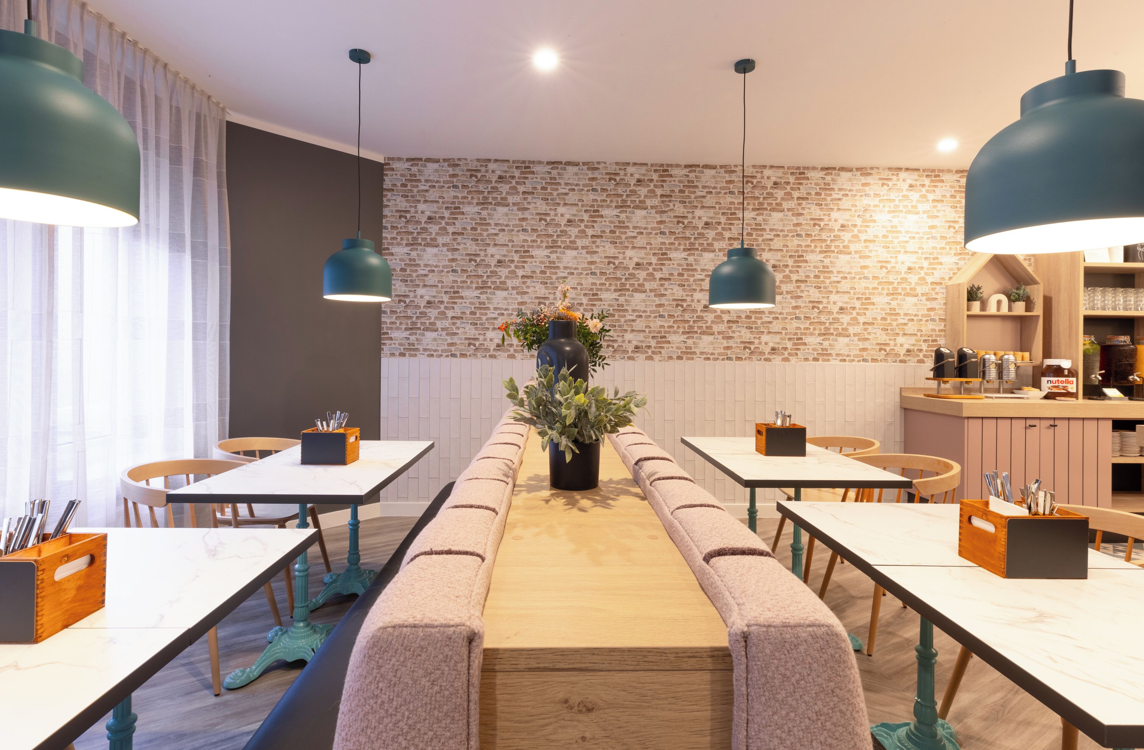 Un comedor moderno con mesas comunitarias largas, bancos y lámparas colgantes.
