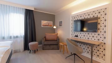 A modern hotel room with a bed, a desk, a chair, and a TV mounted on a geometric-patterned wall.