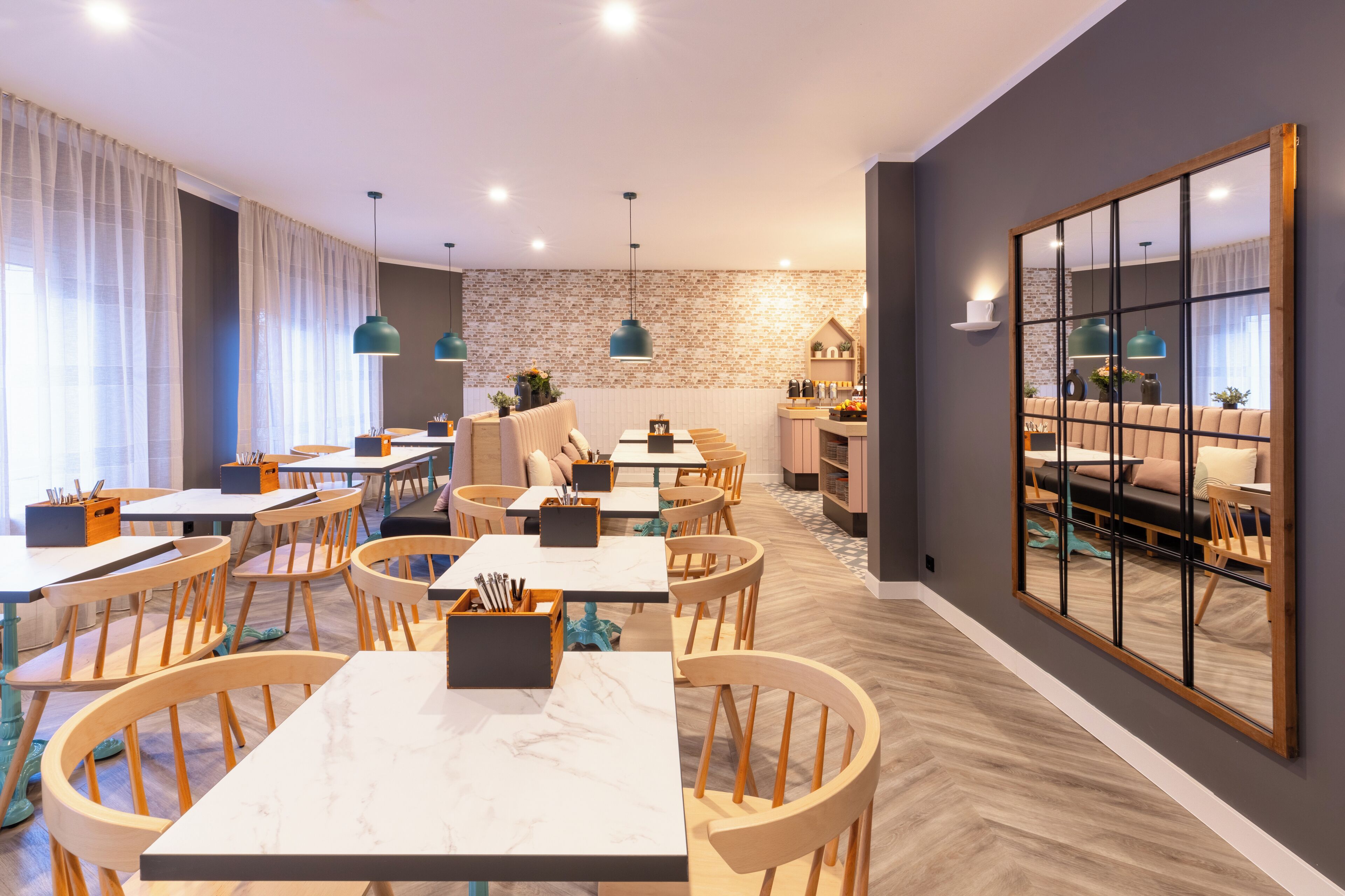 A modern dining area with wooden tables and chairs, a brick-patterned wall, and pendant lighting.
