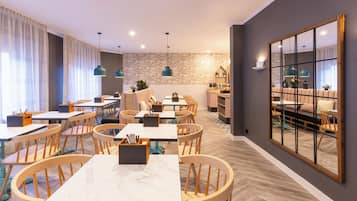 A modern dining area with wooden tables and chairs, a brick-patterned wall, and pendant lighting.