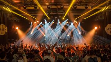 A concert with a crowd facing a stage under bright stage lights.