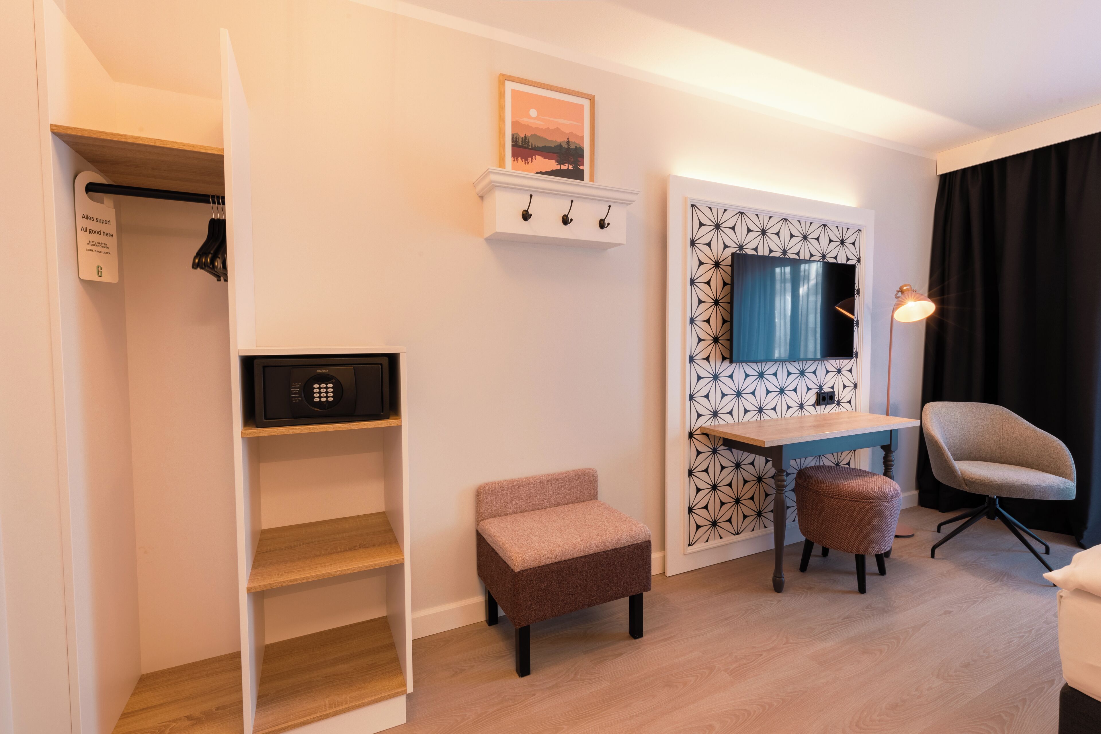 A modern room with a wooden desk, a chair, a small ottoman, a coat rack, and a microwave.