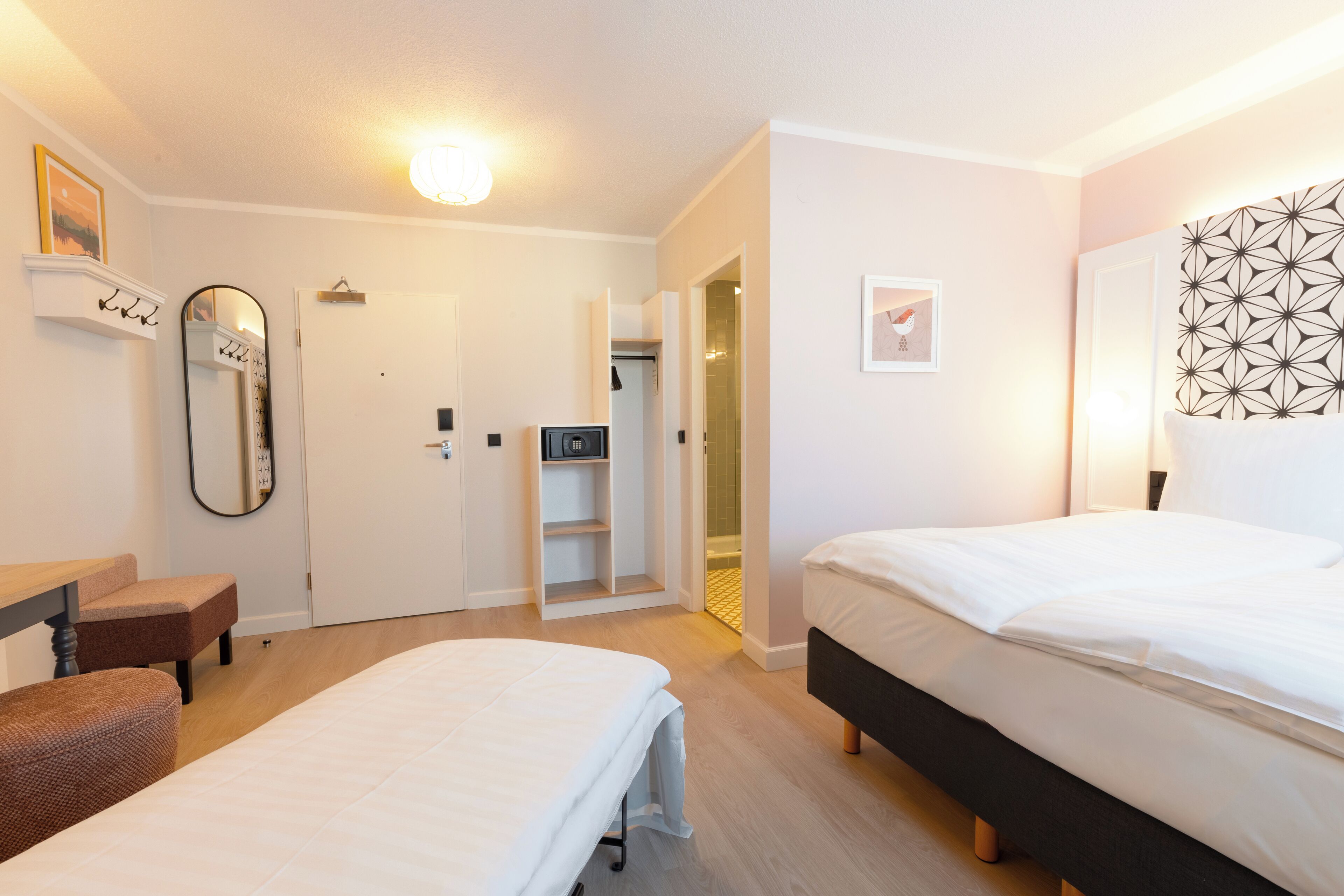 A bedroom with two beds, a desk, a chair, a wardrobe, and a mirror.