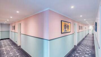 A hotel corridor with a geometric patterned carpet, pastel-colored walls, and framed artwork on the walls.