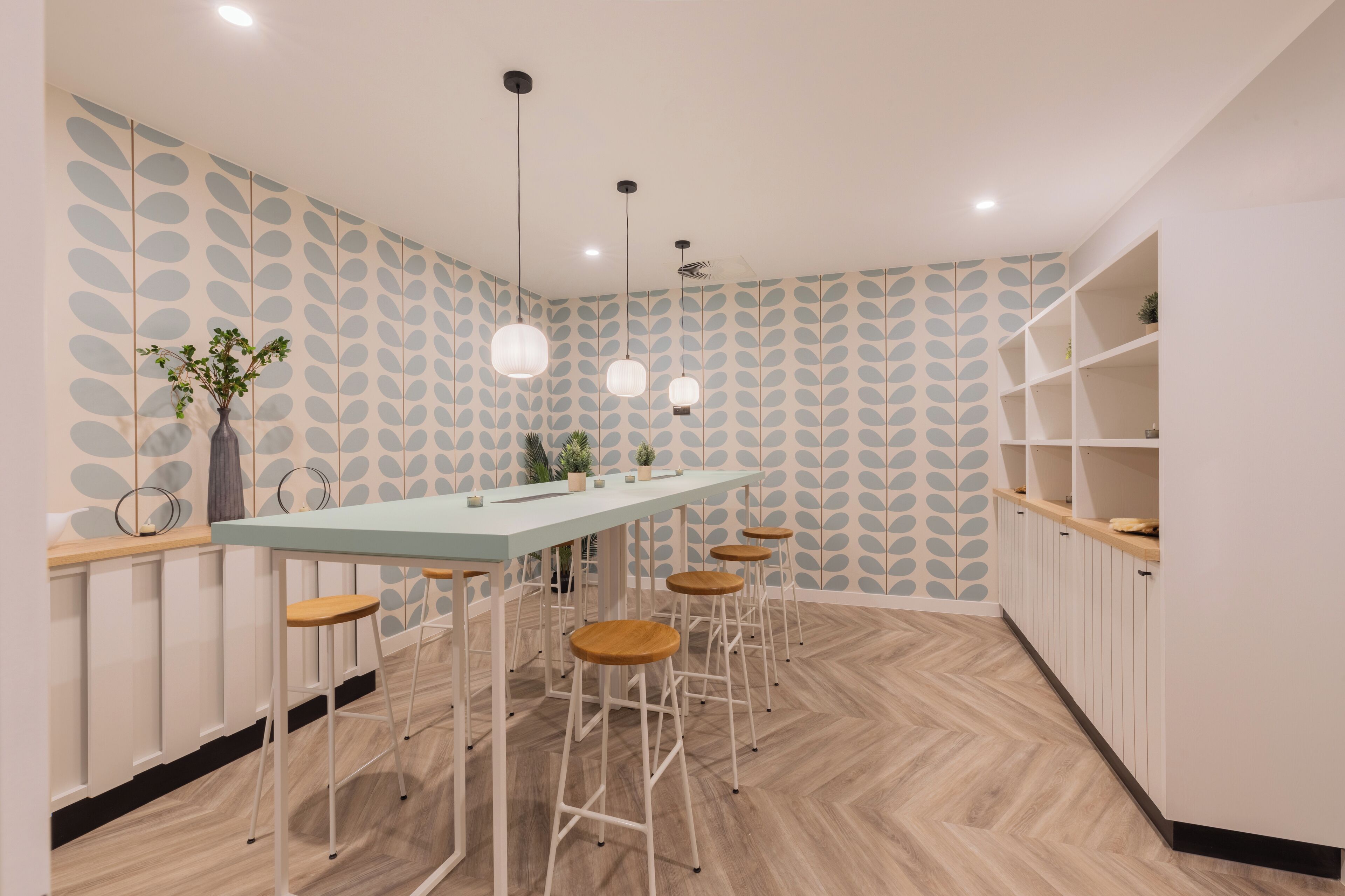 Une cuisine moderne dotée d’un long comptoir, de tabourets de bar, de luminaires suspendus et d’un papier peint à motifs.