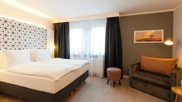 Een hotelkamer met een bed, een bank, een klein krukje, een wandlamp en een schilderij.