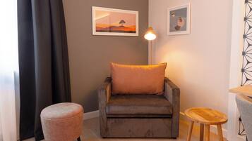 A cozy room with a sofa, a small ottoman, a wooden stool, and two framed pictures on the wall.