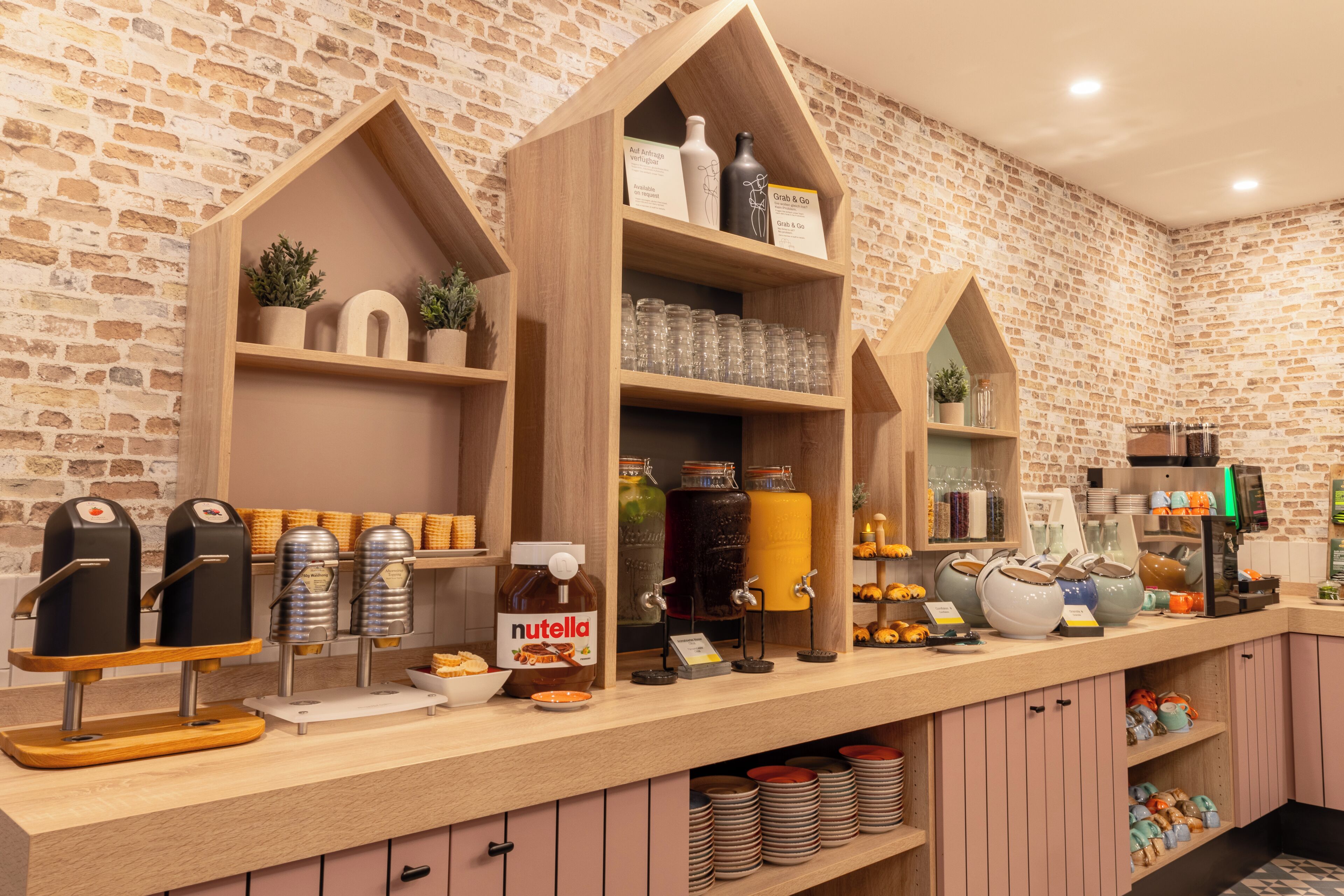 A café with wooden shelves displaying various food items and condiments, including jars of Nutella and other spreads.