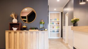 A reception desk with a mirror, a vase with dried plants, and a shelf with books and a water dispenser. - Garner Hotel Mannheim City by IHG (Mannheim)
