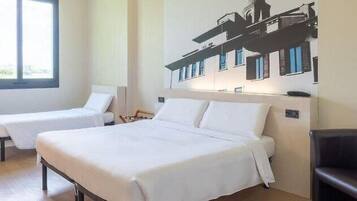 Ein Hotelzimmer mit zwei Betten, einem mit Vorhängen versehenen Fenster und einem an der Wand hängenden Bild eines Gebäudes.