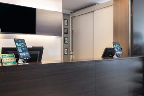 Una recepción de hotel con un televisor de pantalla plana montado arriba, dos quioscos digitales y un cartel con el nombre del hotel.