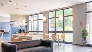Un vestíbulo de hotel moderno con un sofá de cuero negro, una zona de bar y ventanas amplias que ofrecen vistas al exterior.