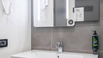 Ein Badezimmer mit einem weißen Waschbecken, einem Spiegel, einem an der Wand hängenden Handtuch und einer Handseifenflasche.