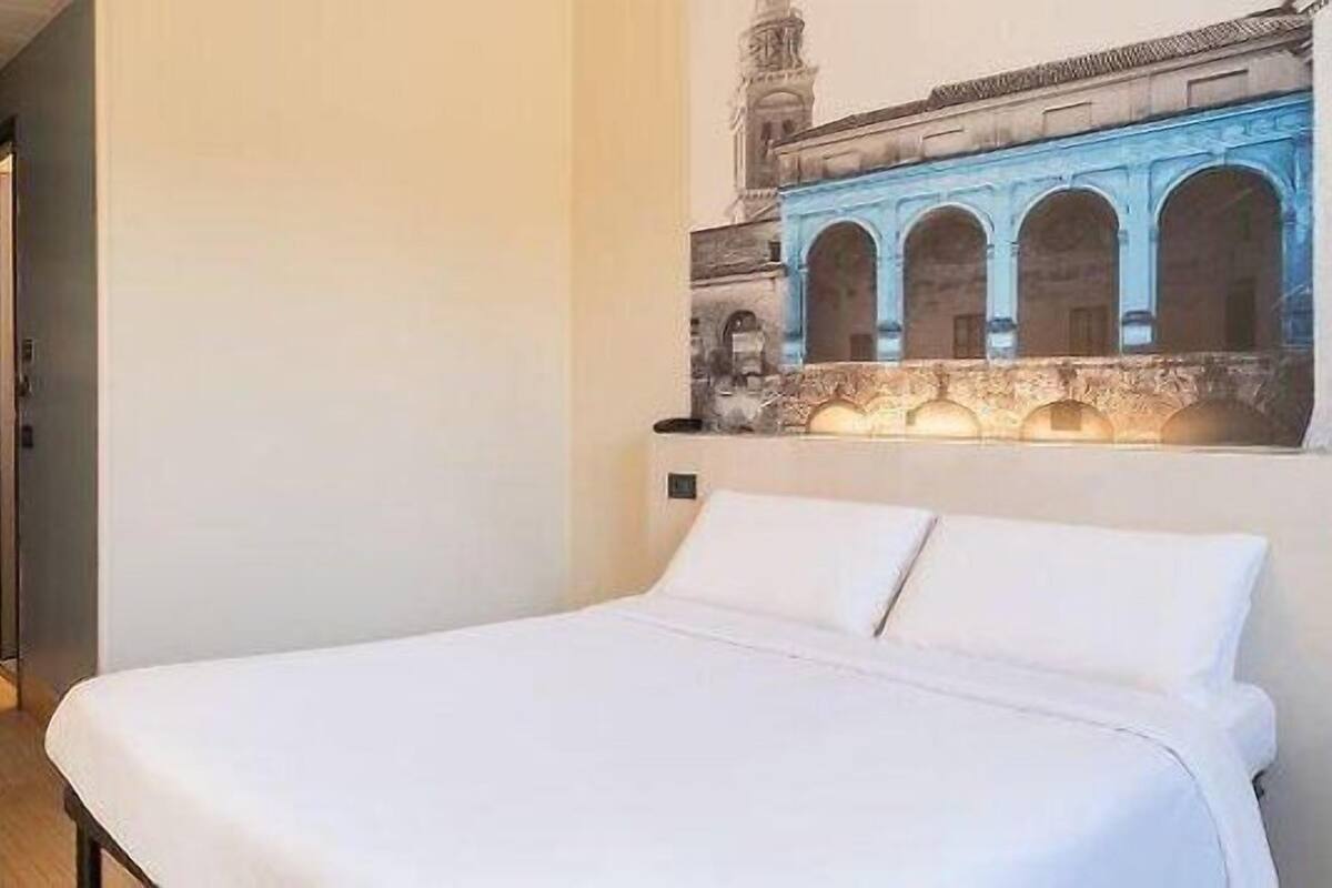 A hotel room with a bed, a door, and a wall mural of a building.