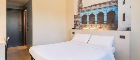 A hotel room with a bed, a door, and a wall mural of a building.