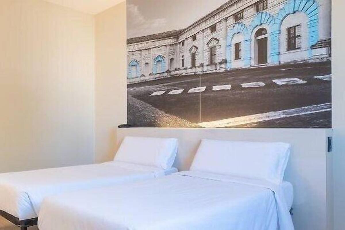 A hotel room with two single beds, a door, a chair, and a wall-mounted picture of a building.