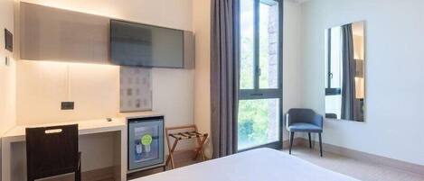 Una habitación de hotel moderna con cama, escritorio con computadora, televisor montado en la pared y ventana con cortinas.