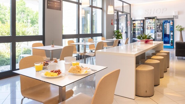 Un comedor moderno con ventanas amplias, una isla central con asientos y una tienda visible al fondo.