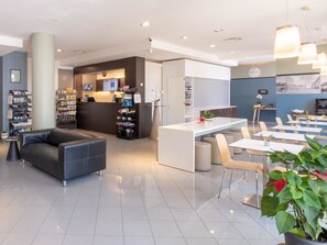 A modern hotel lobby with a reception desk, seating area, and dining space. - B&B Hotel Mantova (San Giorgio di Mantova)