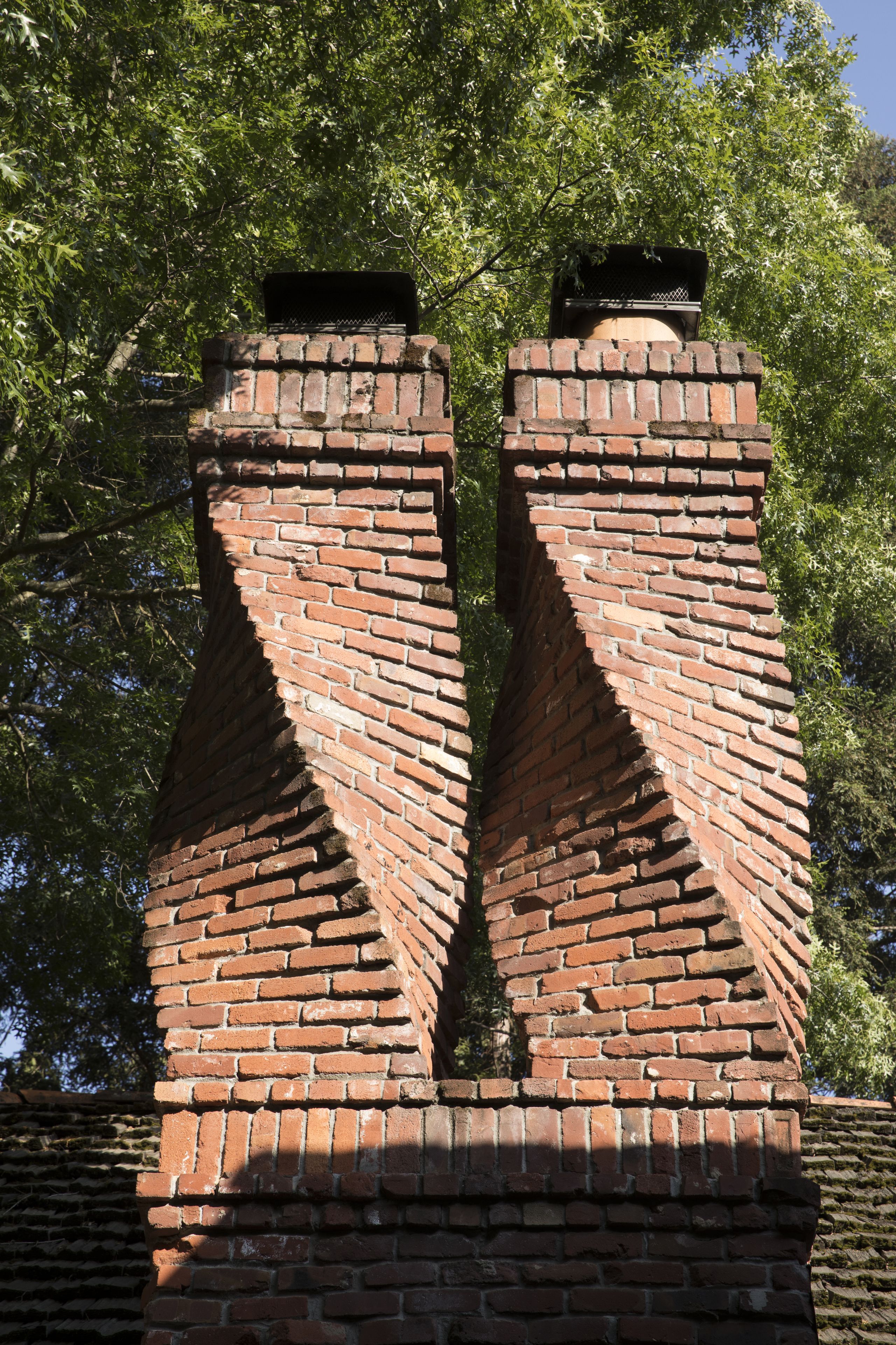 A brick chimney structure with a symmetrical design, surrounded by trees.