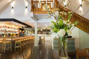 A bar area with a long counter, bar stools, and a staircase in the background.