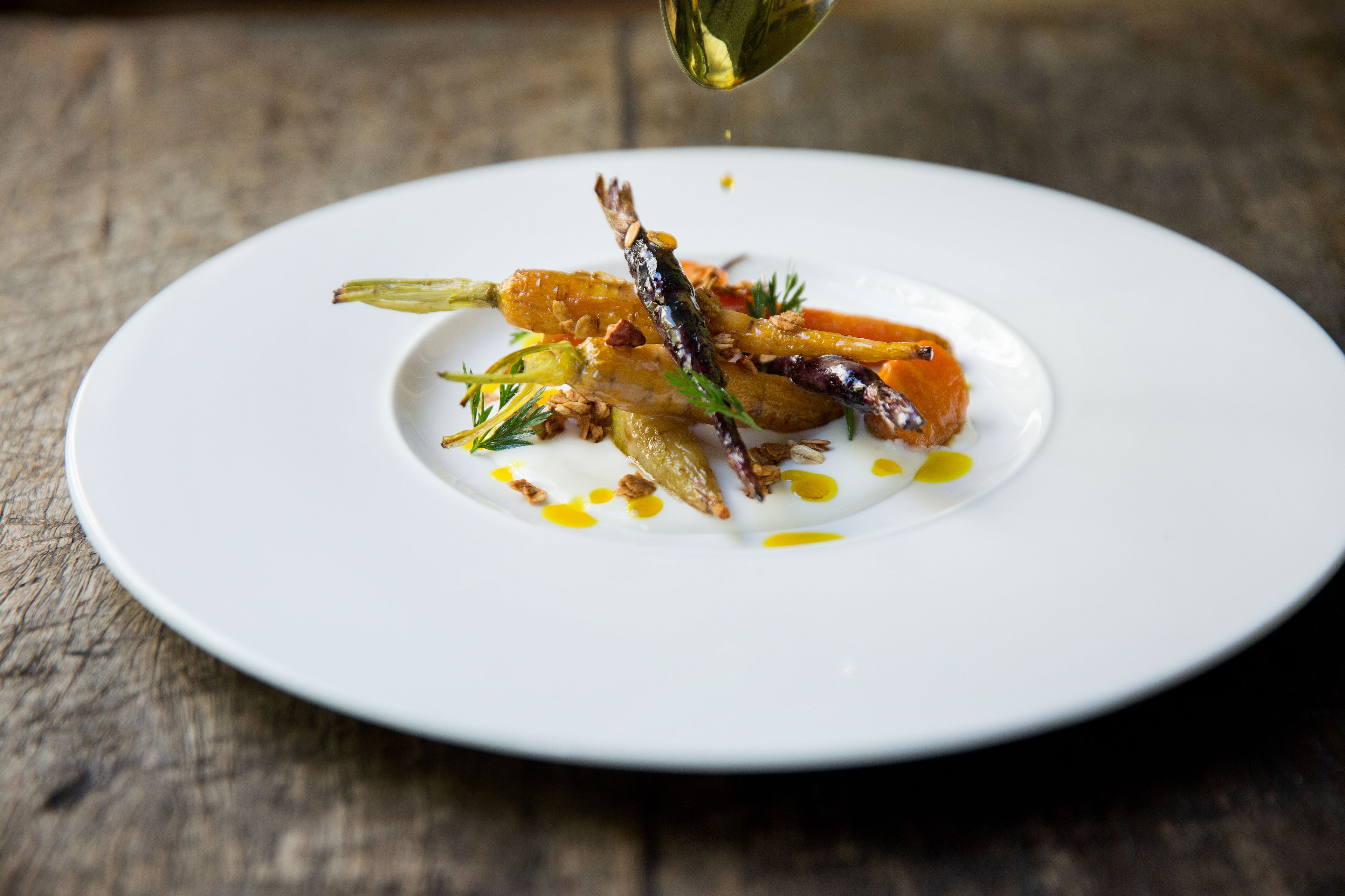 A white plate with a variety of food items, including vegetables and possibly some meat, arranged on a wooden surface.